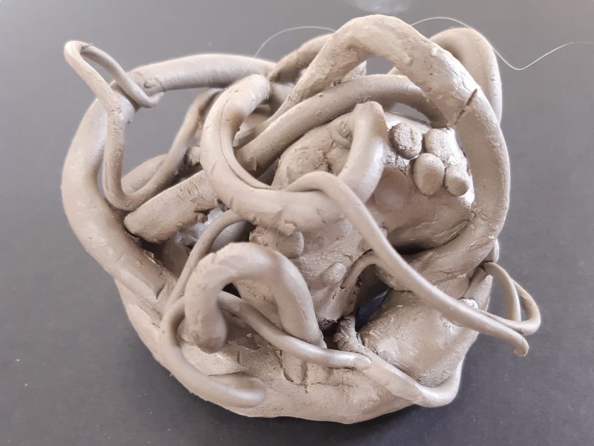 Small clay sculpture by Don: coils of grey clay loop and tangle around a rounded central form, on black card